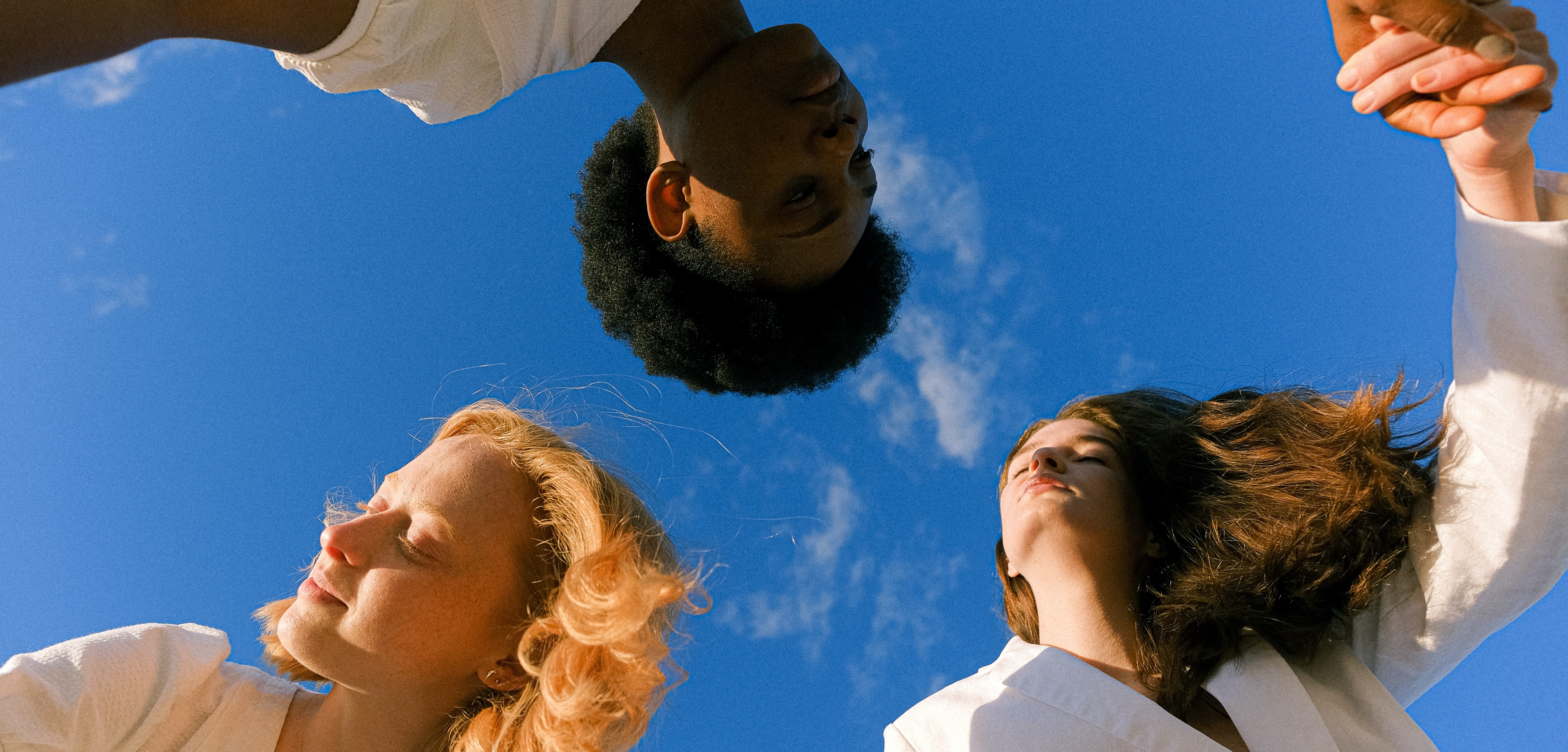 Drei Menschen tanzen unter blauem Himmel